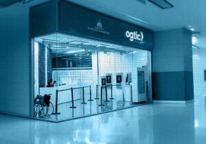 Vista de oficina de atención de OGTIC con mostradores de servicio, quioscos digitales y una silla de ruedas en la entrada.